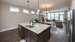 A modern kitchen with a large island, dark wood cabinets, and pendant lighting.