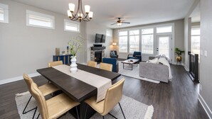 A spacious living area with a dark wood dining table, beige chairs, a fireplace, and a ceiling fan.