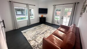 A modern living room with a brown leather sofa, a patterned rug, and a flat-screen TV on the wall. - Charming backyard Guesthouse with 2 bedrooms and WiFi, AC in Pleasant Hill (Pleasant Hill)