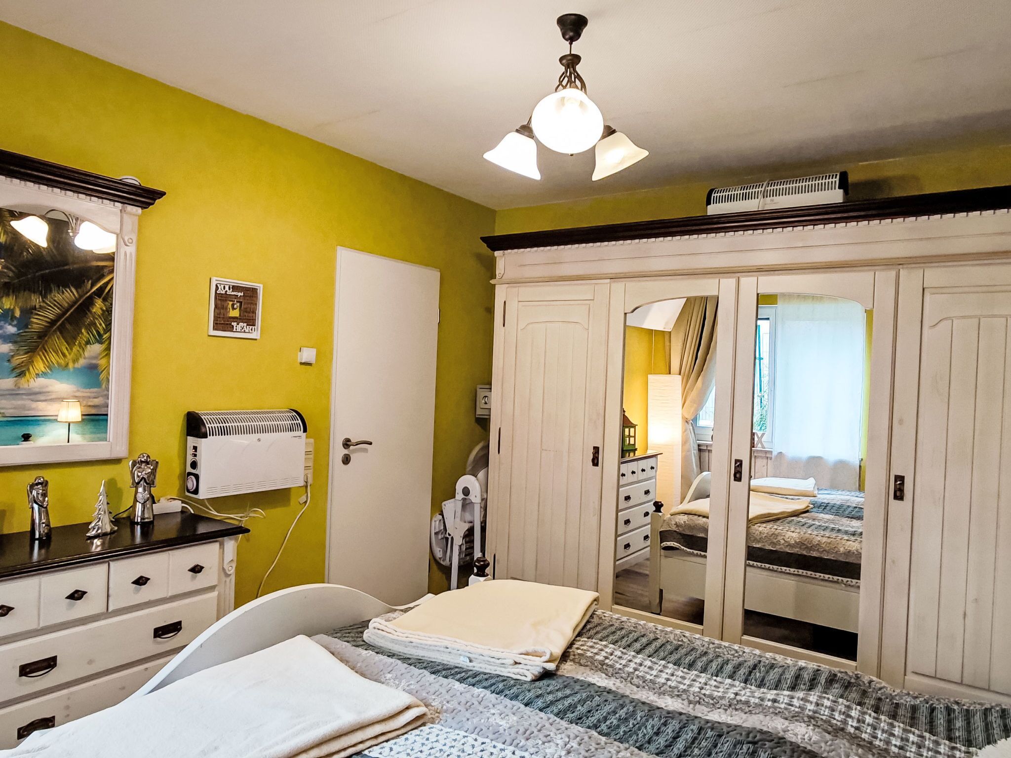 Un dormitorio con cama, cómoda, espejo, ventilador de techo y armario.