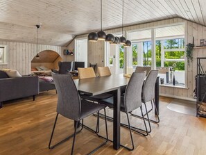 A modern interior with a dining area, a sofa, and a view of greenery outside.