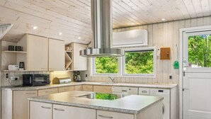 Una cocina moderna con una isla central, electrodomésticos integrados y vistas a zonas verdes a través de las ventanas.