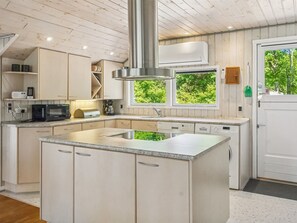 A modern kitchen with a central island, built-in appliances, and a view of greenery through the windows.