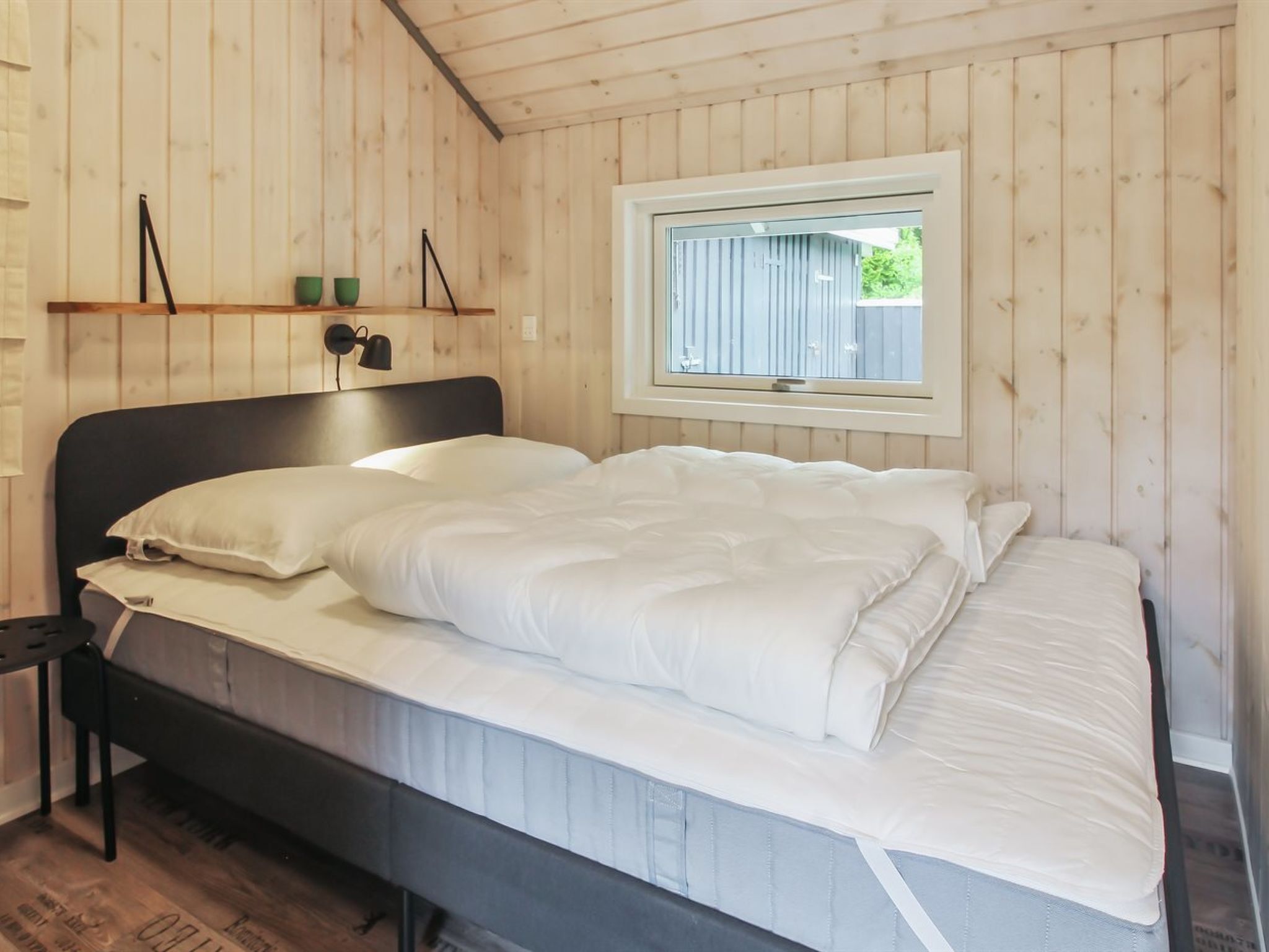 A bed with white bedding in a room with wooden walls and a window.