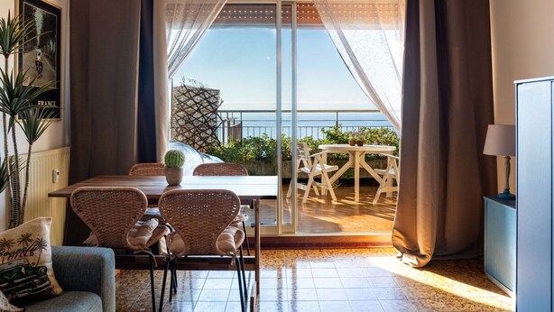 A room with a dining table, chairs, a sofa, and a view of the sea through large windows. - Nice apartment for 3 people with WIFI and pets allowed (Ventimiglia)
