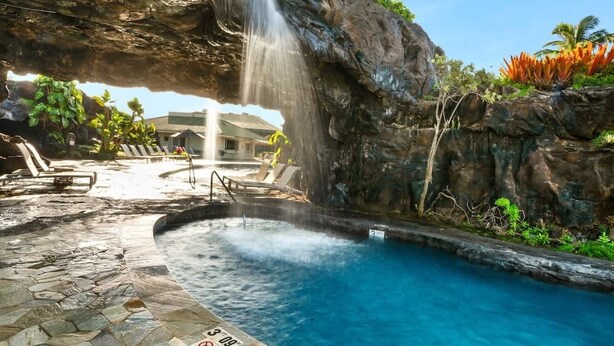 A pool area with a waterfall feature, lounge chairs, and a tropical setting.