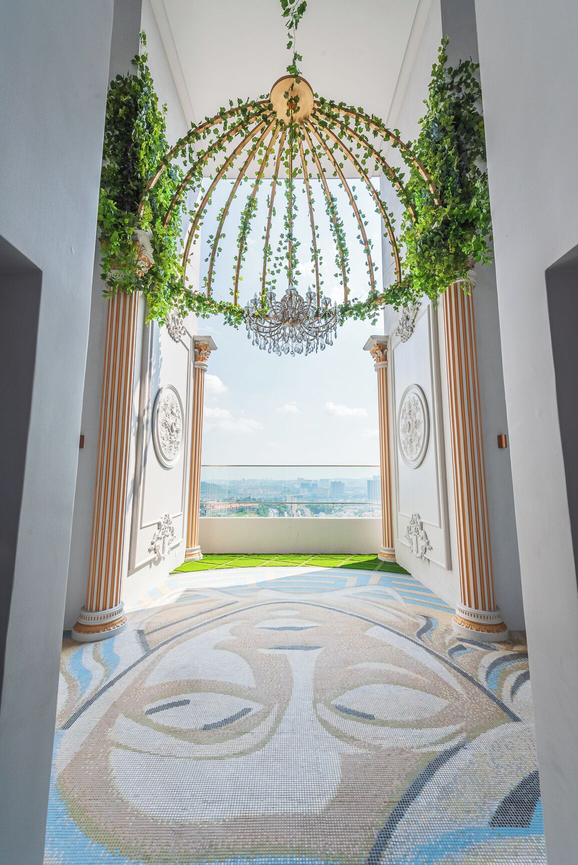 A corridor with a view to the sea, columns, a chandelier, and a patterned floor.
