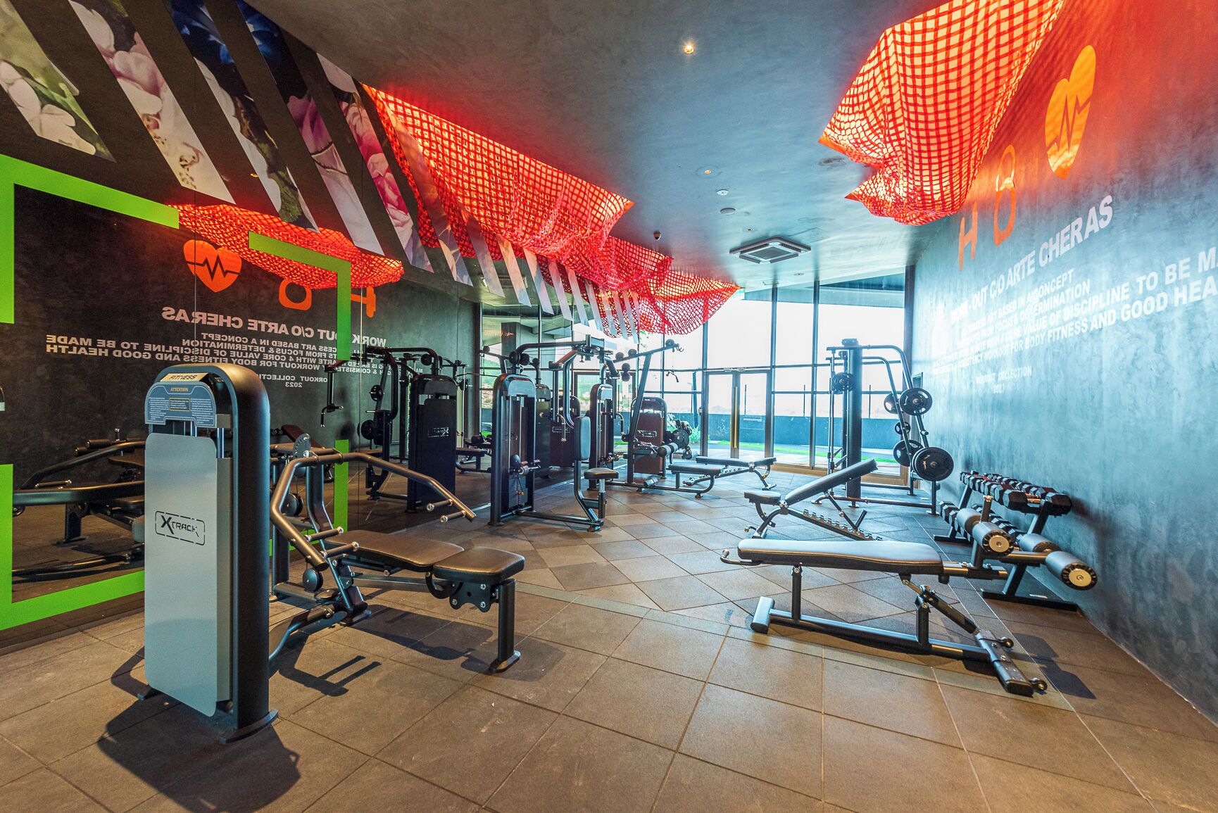 A gym with various exercise equipment, large windows, and motivational posters on the walls.
