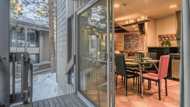 A modern kitchen with a dining area, featuring a glass door entrance, a wooden deck, and a tiled floor.