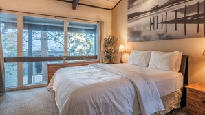 A bedroom with a large bed, a nightstand, a lamp, and a window with a view of trees.