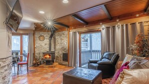 A cozy living room with a fireplace, a leather sofa, a patterned rug, and a stone wall.