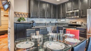 A modern kitchen with dark cabinets, stainless steel appliances, and a glass dining table set for four.