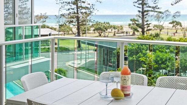 A balcony with a table, a bottle of Cosmopolitan, a glass, and a fruit. - Luxury Beachfront Stay in Kirra (Coolangatta)