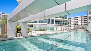 A modern swimming pool with clear water, surrounded by white lounge chairs and a contemporary building with large windows. - Luxury Beachfront Stay in Kirra (Coolangatta)
