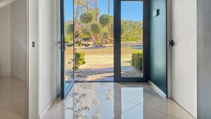 Un pasillo moderno con una puerta de cristal que da a un espacio exterior con árboles y cielo despejado.