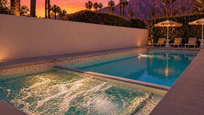 Una piscina con vista a las montañas, rodeada de palmeras y sillas de descanso.