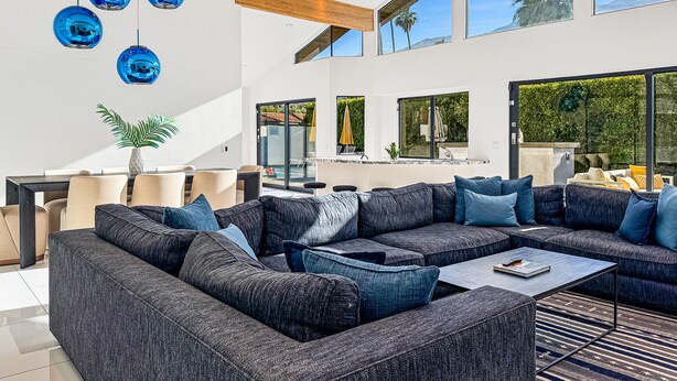 Una sala moderna con un sofá seccional, un comedor y ventanas amplias con vistas al exterior.