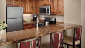 A kitchen with wooden cabinets, a stainless steel refrigerator, a microwave, a coffee maker, and a granite countertop. - VAIL Luxury 2BR Villa ~ Marriott’s Streamside (Vail)