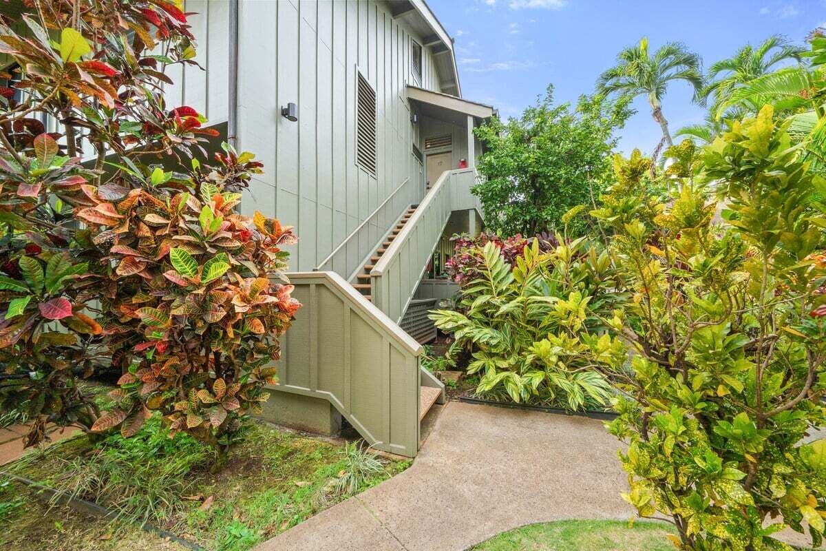 Un edificio con una escalera que conduce a un balcón, rodeado de plantas y árboles.