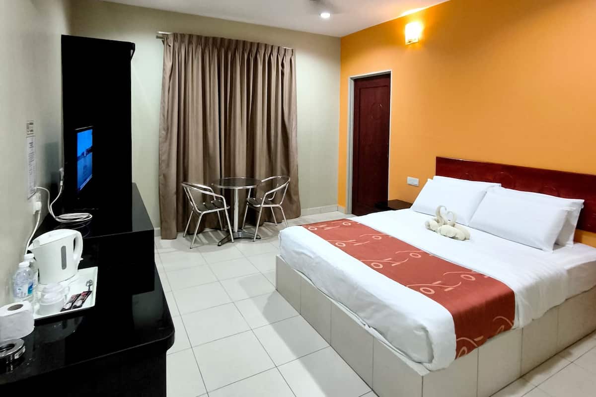 Ein Hotelzimmer mit einem Bett, einem Schreibtisch mit Computer, einem Sessel, einem Tisch und einem Deckenventilator.