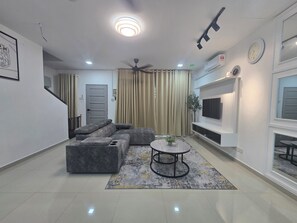 Un salon moderne avec un canapé d’angle, une table basse ronde et un téléviseur à écran plat fixé au mur.