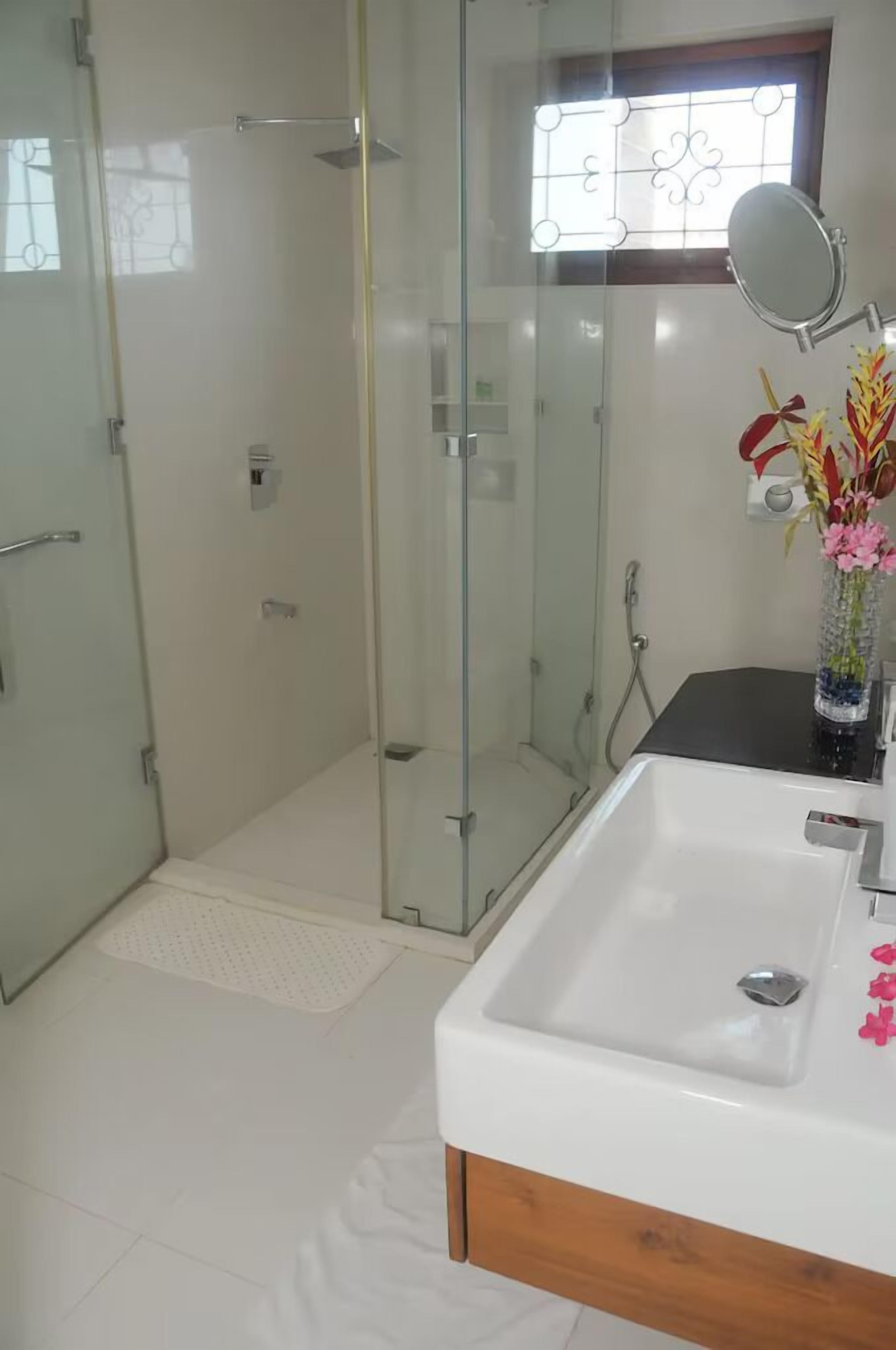 A modern bathroom with a glass-enclosed shower, a white sink, and a mirror.
