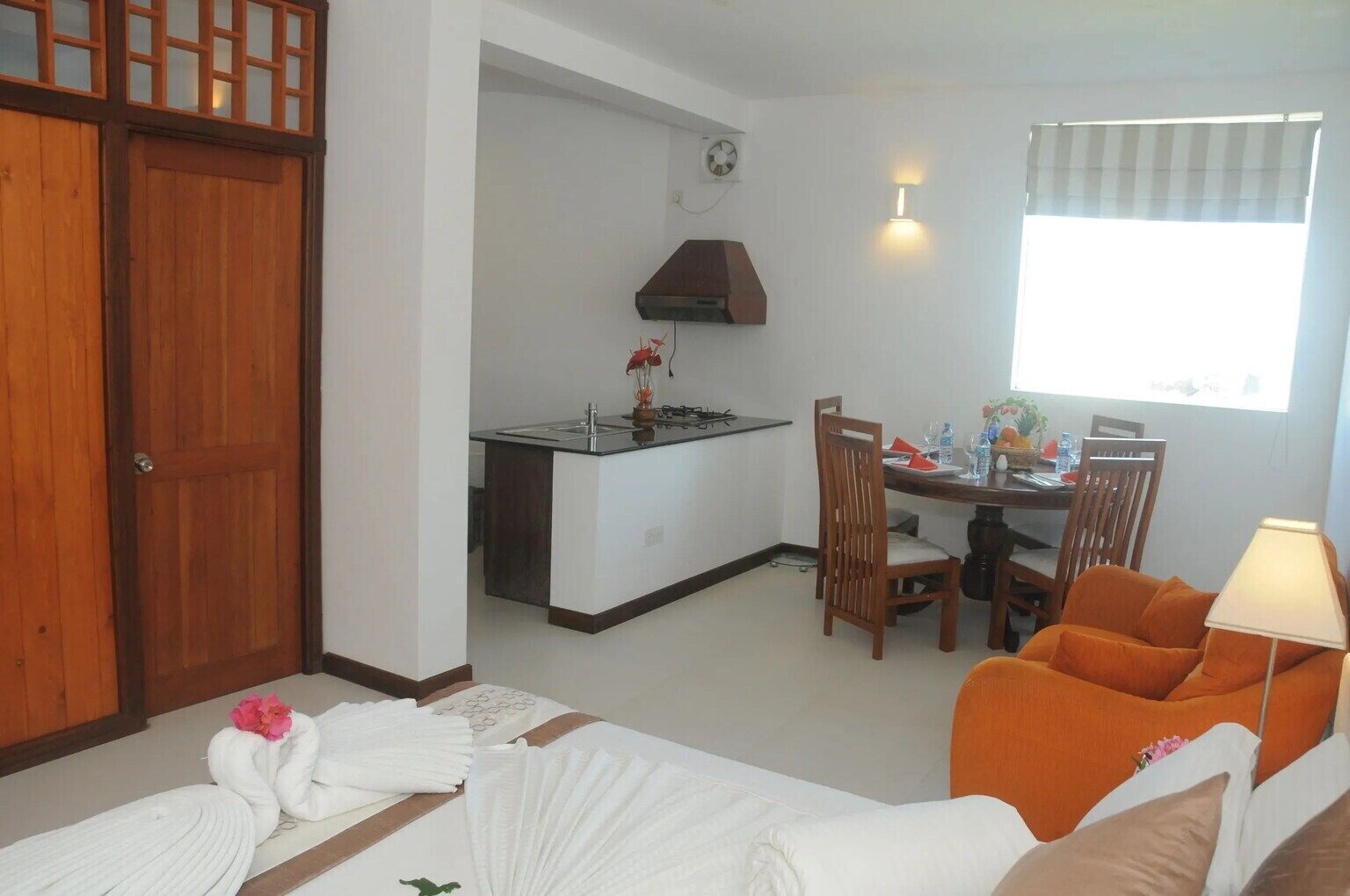 Quarto de hotel com cama, mesa de jantar e cadeiras, cozinha e janela com persianas.