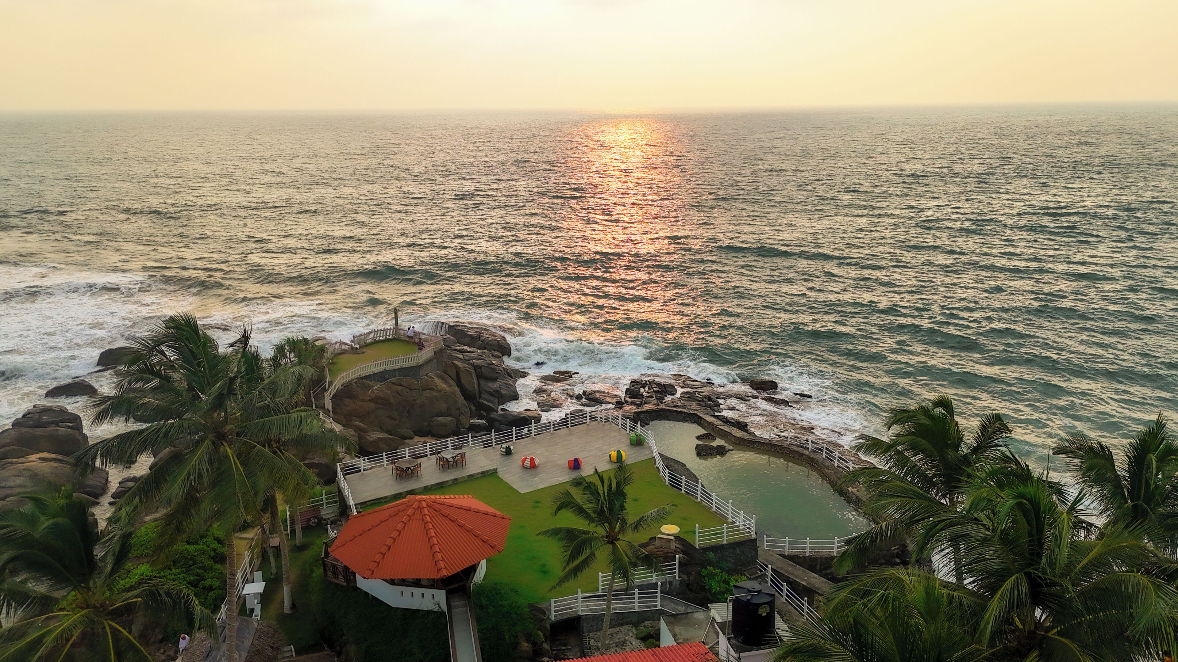 Un resort costero con piscina, palmeras y vista al océano al atardecer.