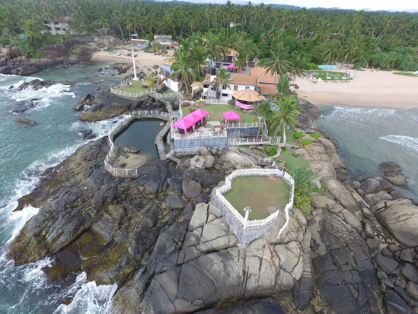 A coastal resort with rocky terrain, a swimming pool, and a beach area.
