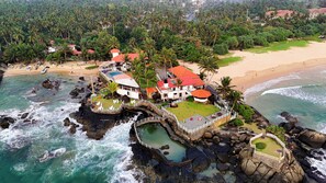 A coastal resort with multiple buildings, a rocky shoreline, and a beach. - Scarlet White Resort (Ahungalla)