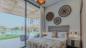 A bedroom with a large bed, a nightstand, a lamp, and a view of an outdoor swimming pool. - Villa PurSang Marrakech – Villa Privée de Luxe avec Hammam, Spa et Jardin (Marrakech)