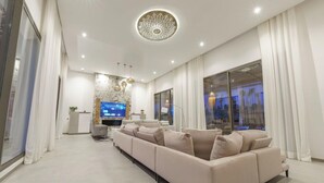 A modern living room with a large beige sofa, a flat-screen TV, and a decorative ceiling light. - Villa PurSang Marrakech – Villa Privée de Luxe avec Hammam, Spa et Jardin (Marrakech)