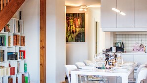 A modern kitchen with white cabinets, a dining area with white chairs, and a staircase with wooden railings. - Bietschorn 20 by Interhome (Nendaz)