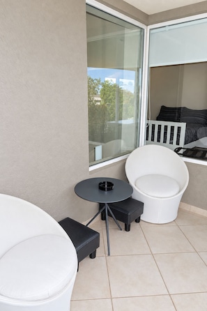 A balcony with a white chair, a small round table, and a white sofa.