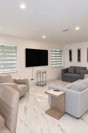 A modern living room with a flat-screen TV, two sofas, a coffee table, and a glass side table.