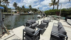 A waterfront patio with outdoor furniture, a pool, and palm trees.