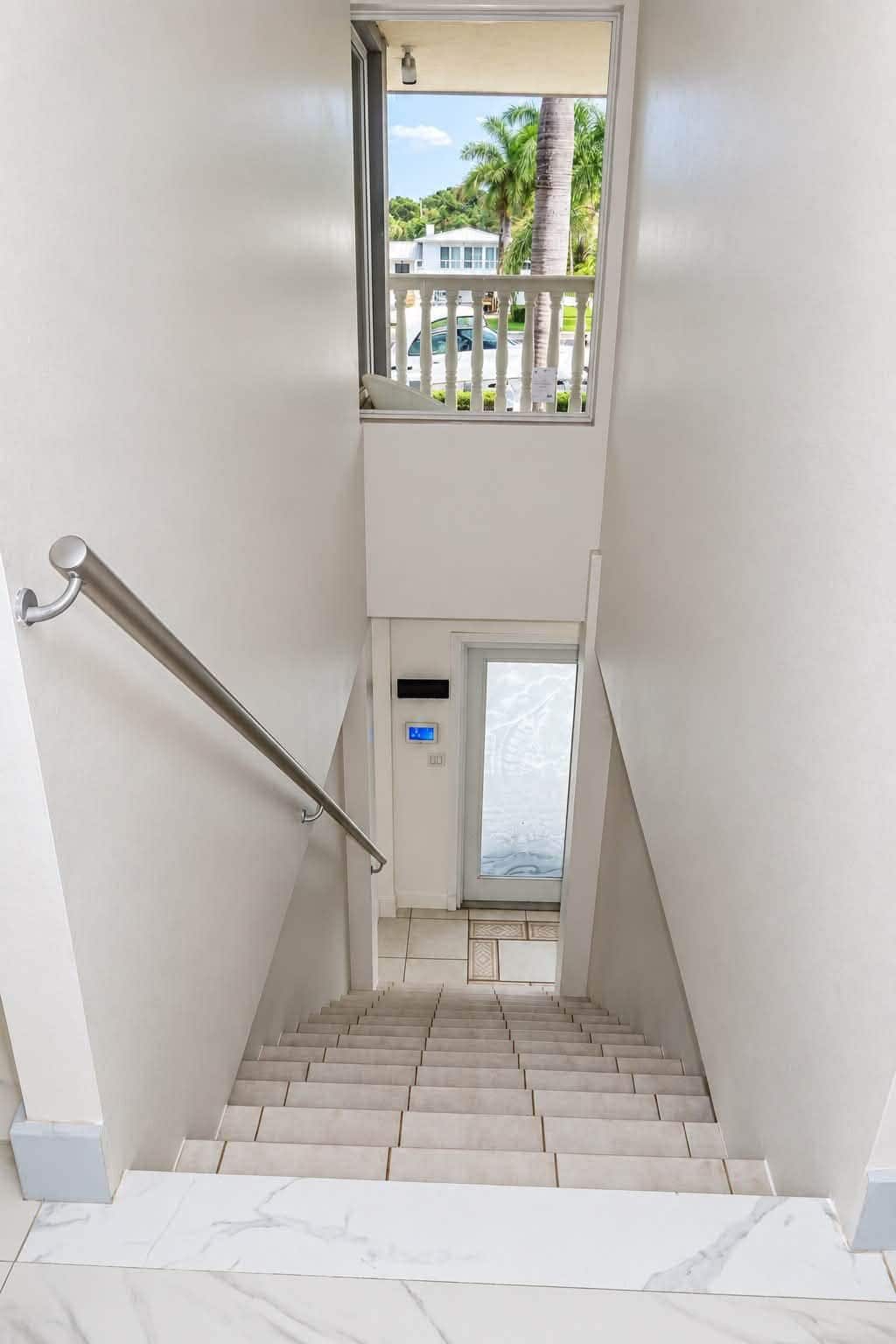 Een trap met een leuning, leidend naar een deur met uitzicht op een palmboom en een witte schutting.