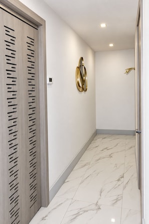 A hallway with a wooden door, a wall-mounted light fixture, and a marble floor.