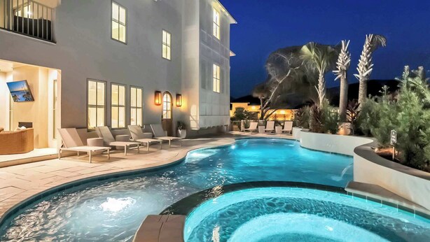 A modern house with a swimming pool, lounge chairs, and a well-lit exterior at night. - Majestic Sands | Free Golf Cart & Beach Chairs | Gorgeous Private Pool & Courtyard | 2 PM Check In! | Clubhouse Amenities! Pickleball, Gym & Hot Tub! (Destin)