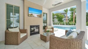 A modern outdoor living area with wicker furniture, a fireplace, and a pool view. - Majestic Sands | Free Golf Cart & Beach Chairs | Gorgeous Private Pool & Courtyard | 2 PM Check In! | Clubhouse Amenities! Pickleball, Gym & Hot Tub! (Destin)