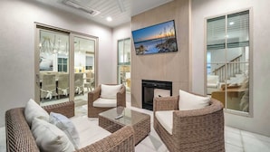A modern living room with wicker furniture, a fireplace, and large windows offering views of the interior and exterior. - Majestic Sands | Free Golf Cart & Beach Chairs | Gorgeous Private Pool & Courtyard | 2 PM Check In! | Clubhouse Amenities! Pickleball, Gym & Hot Tub! (Destin)