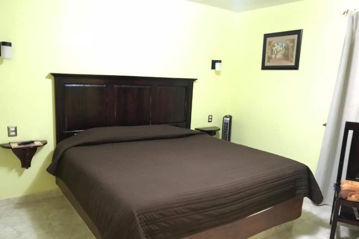 Une chambre à coucher avec un grand lit, une table de chevet, une lampe fixée au mur et un tableau accroché au mur.