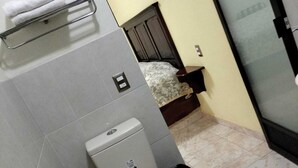 Casa de banho com sanita, um porta-toalhas, cama e zona de duche.
