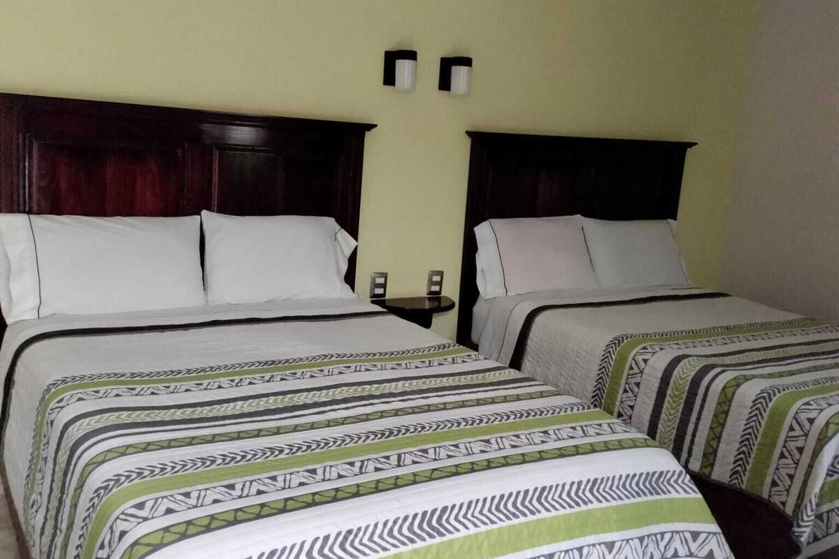 Une chambre d’hôtel avec deux lits, chacun agrémenté de draps à motifs et d’une tête de lit sombre.