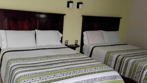 Quarto de hotel com duas camas, cada uma com roupa de cama estampada e cabeceira escura.