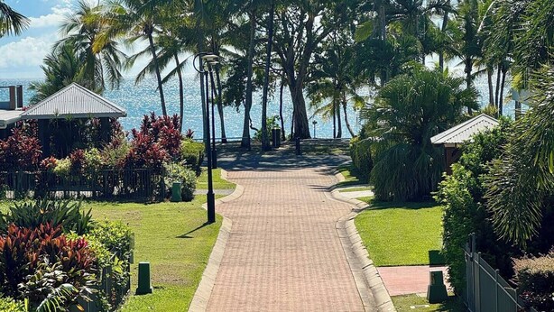 A pathway leading to a building with a tiled roof, surrounded by palm trees and well-maintained greenery.
