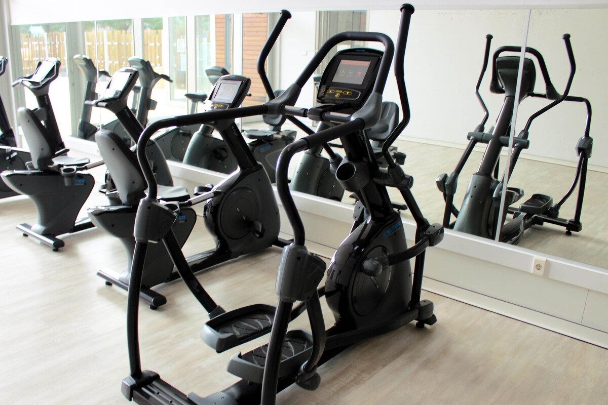 A gym with various exercise machines, a large mirror, and a wooden floor.