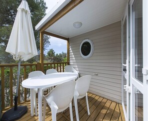 A covered outdoor area with a table and chairs, a white umbrella, and a view of the surrounding trees.