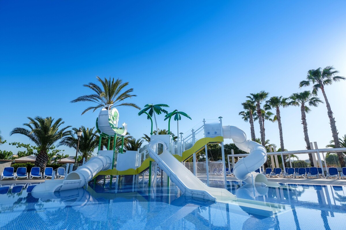 A swimming pool with a water slide, palm trees, and lounge chairs.