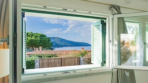 A room with a window overlooking a scenic view of a lake, a wooden deck, and a mountain in the distance. - Appartamento Mare di Spartaia (Marciana)